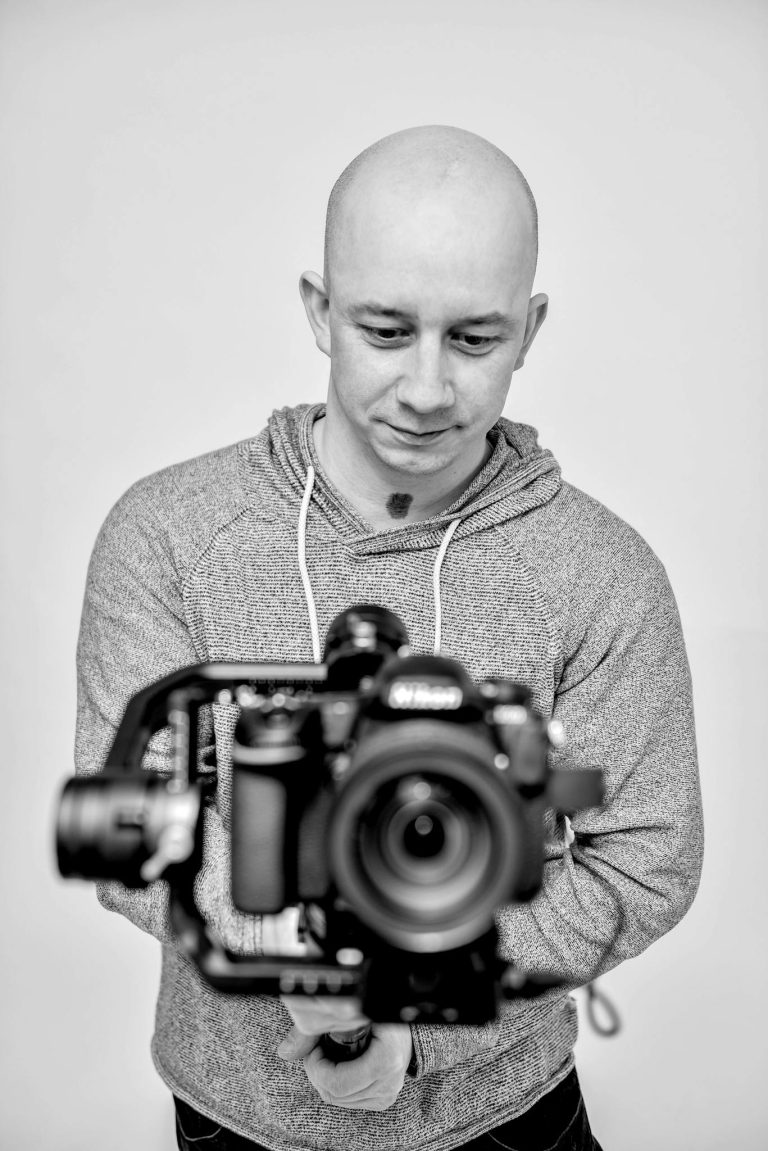 Bald man in gray hoodie using DSLR camera on gimbal. Black and white portrait.